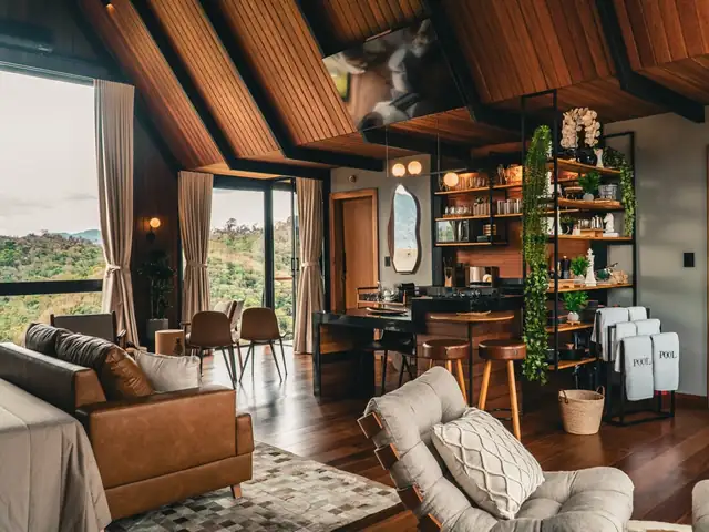 A sala e a cozinha sob o telhado de madeira, com a janela de vidro aberta para a serra
