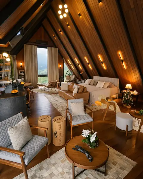 A sala sob o telhado em A de madeira, com a cama ao fundo e as janelas para a serra